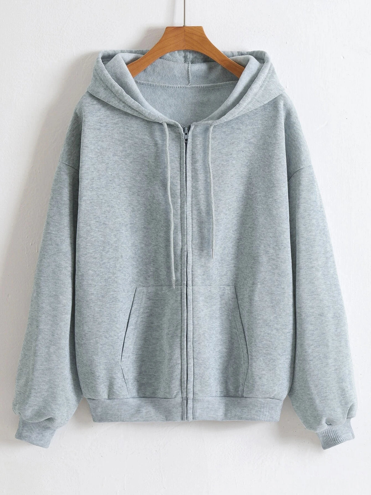 A light gray oversized zip-up hoodie hanging on a wooden hanger.