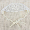 White floral lace baby headband with a gathered bow on a beige fabric background