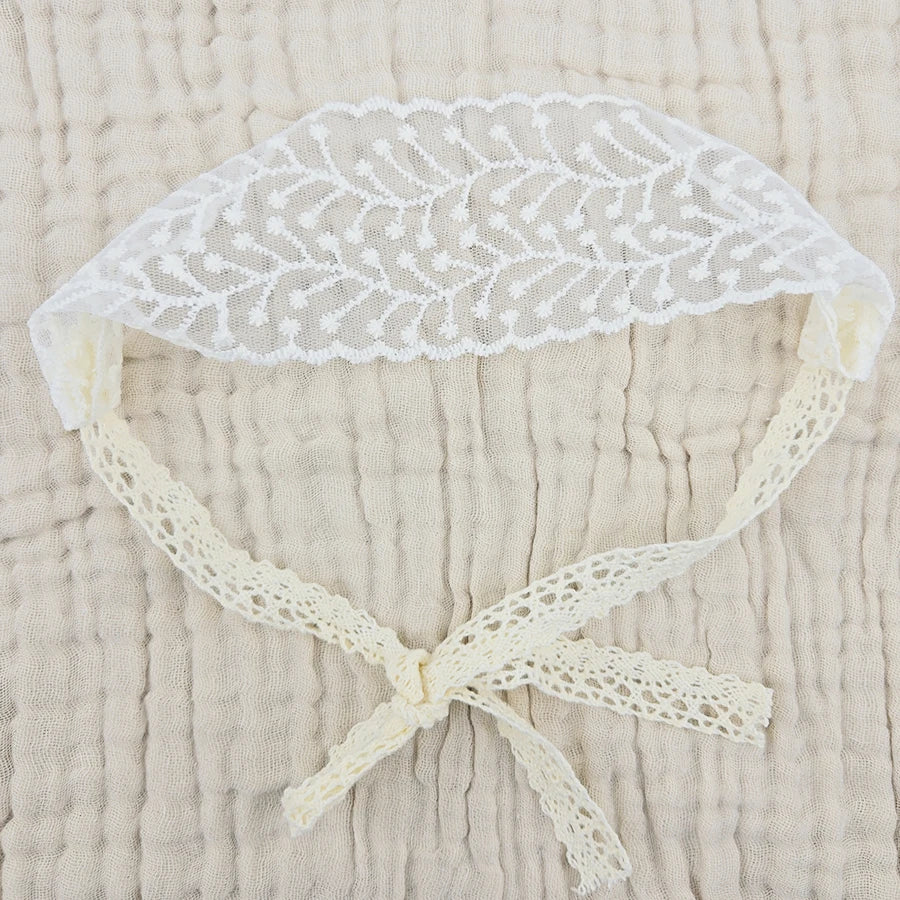White floral lace baby headband with a gathered bow on a beige fabric background