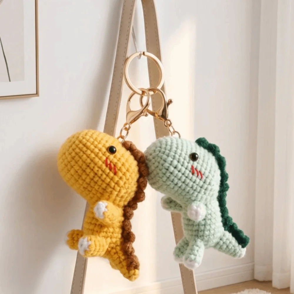 A handmade crochet dinosaur keychain in yellow and green colors hanging on a wooden hanger.