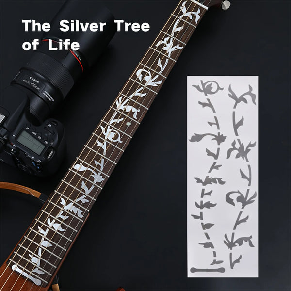 A close-up of a guitar fretboard showing silver tree inlay decals on the wood.