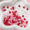 A close-up view of a white dish filled with various colored glass spacer beads including red, pink, and clear beads.