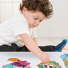 A child is playing with a jumbo-sized puzzle set featuring fairy tales and animals on a white surface.