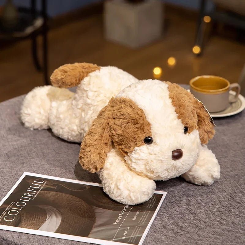 A fluffy, light-colored dog plush toy lying on a gray surface next to a cup.
