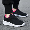 A close-up of a black mesh sneaker with pink accents and white sole, worn on a person's foot.