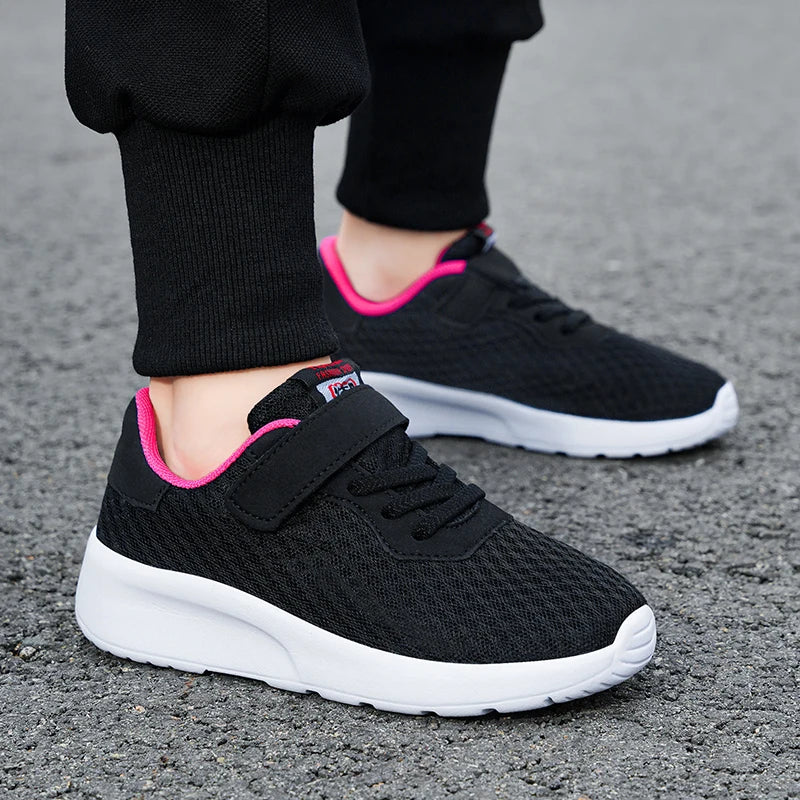 A close-up of a black mesh sneaker with pink accents and white sole, worn on a person's foot.