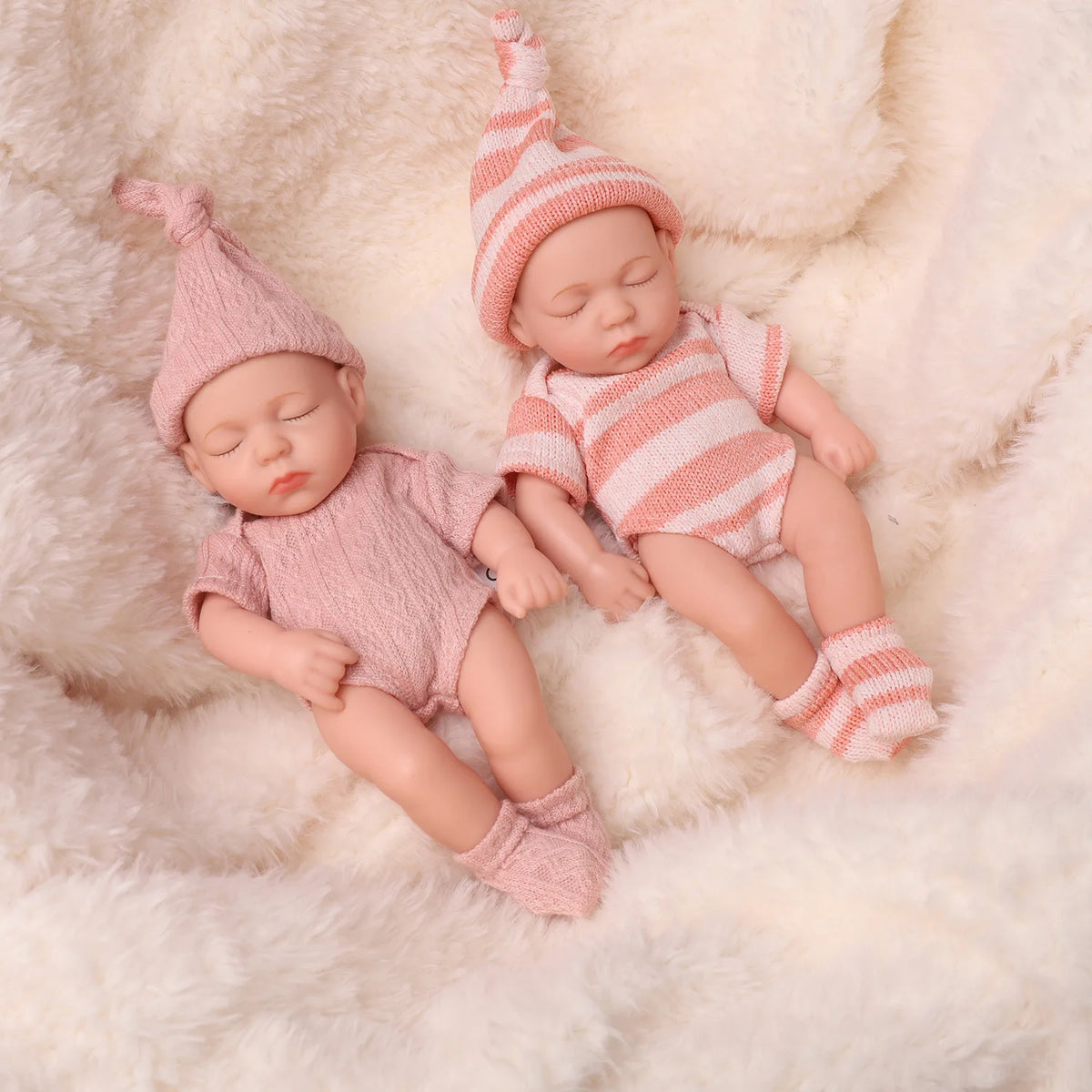 A realistic soft vinyl baby doll wearing a pink striped outfit and matching hat, lying on a fluffy white surface.