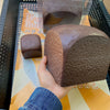 A hand is holding a brown squishy toy shaped like a loaf of bread, packaged in clear plastic.