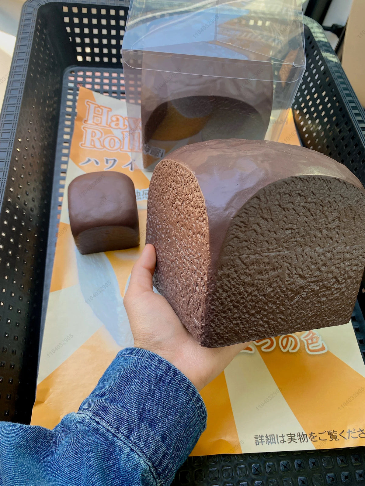 A hand is holding a brown squishy toy shaped like a loaf of bread, packaged in clear plastic.