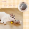 A white cat is playing with a yellow toy on the floor next to a motion-activated hide and seek cat toy.