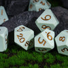 A collection of white silicone polyhedral dice resting on green grass and dark rocks.