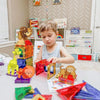 A child is playing with red and blue magnetic building blocks shaped like dinosaur and animal figures.