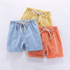 Three pairs of kids cotton-linen summer shorts in light yellow, blue, and coral orange with adjustable elastic waists