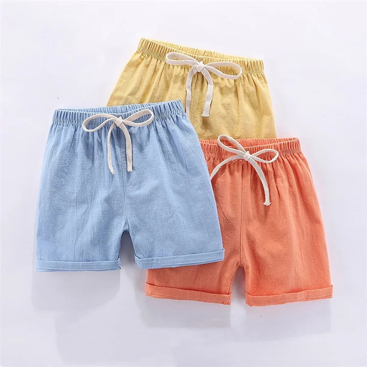 Three pairs of kids summer linen shorts in light yellow, blue, and coral with adjustable elastic waists