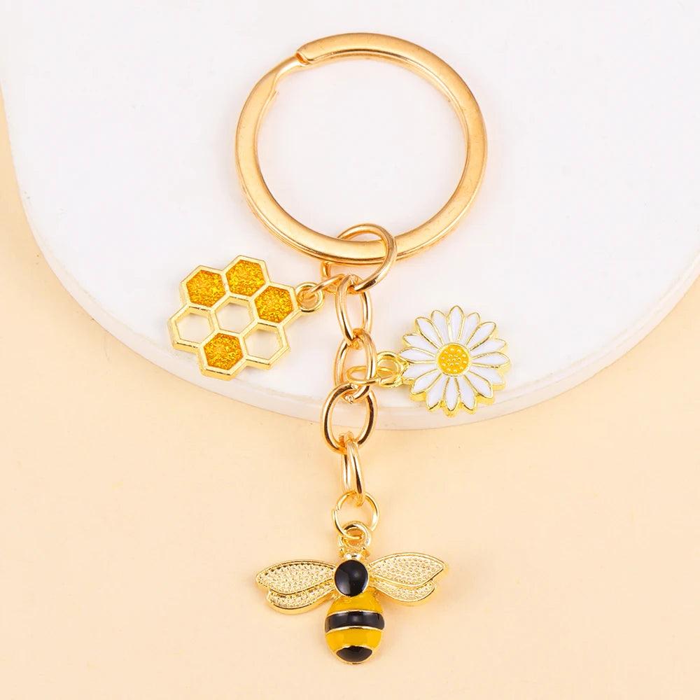 Gold enamel keychain featuring a honeycomb, a daisy flower, and a bee charm.