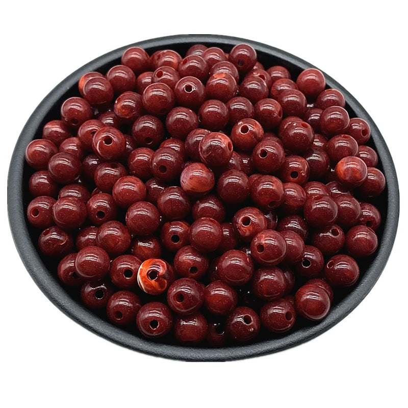 A pile of dark reddish-brown acrylic round beads for jewelry making in a black bowl.