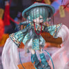 A detailed collectible doll featuring teal hair and clothing, presented in a box set.