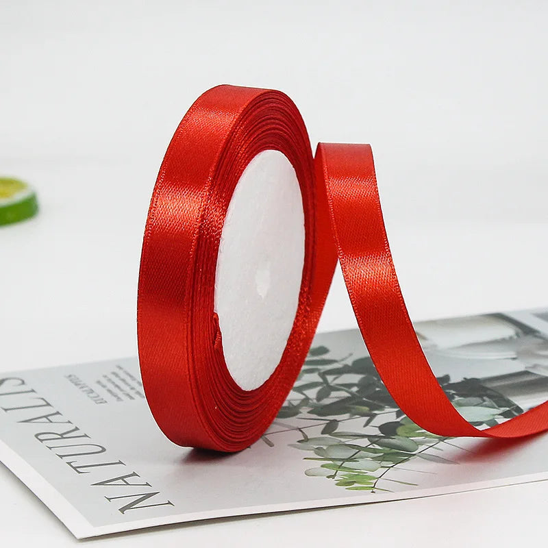 A roll of red satin ribbon for gift wrapping and crafts lying on a white surface.