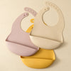 A set of two light pink and cream waterproof silicone baby bibs with adjustable necks displayed against a neutral background.