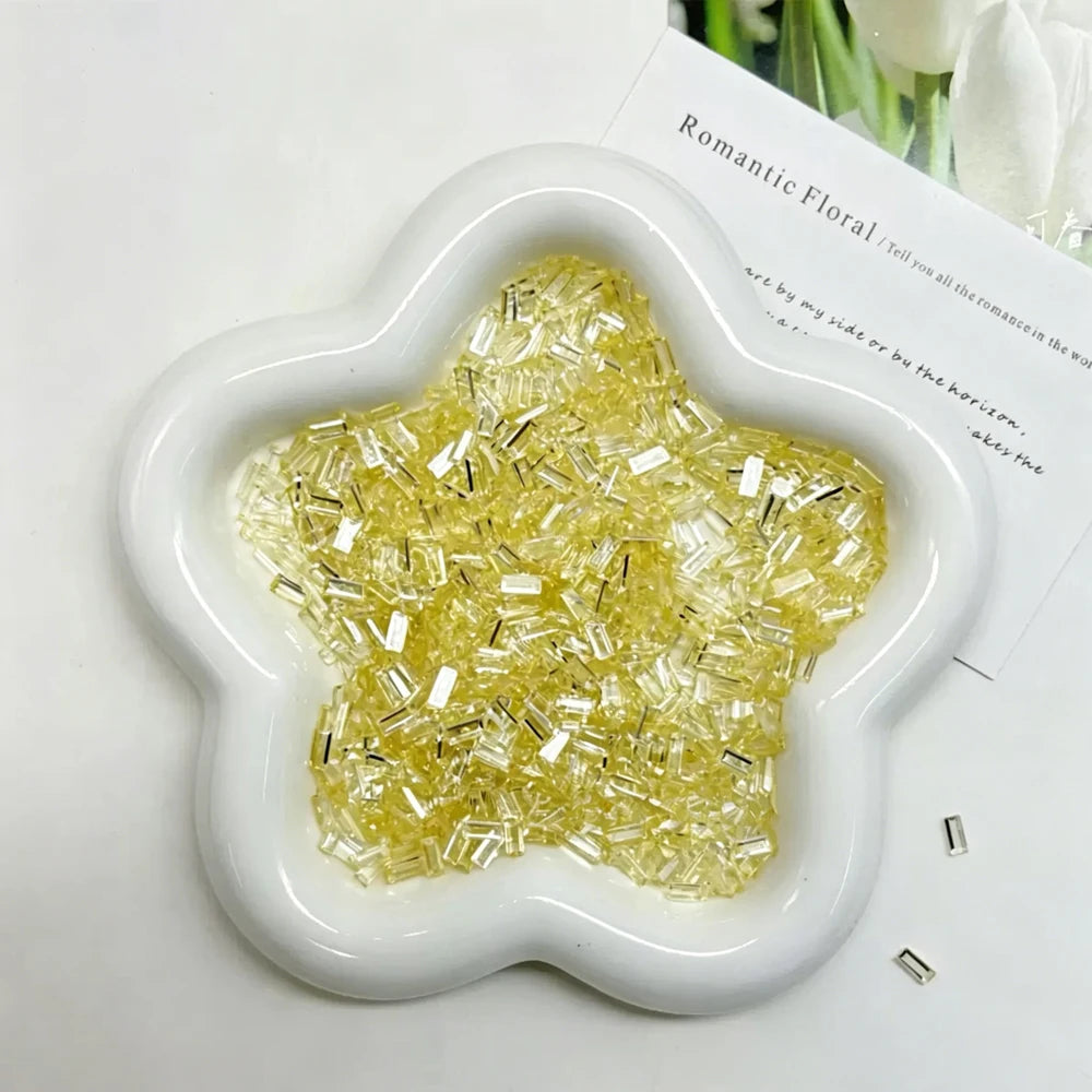 A white flower-shaped mold filled with yellow glitter ice strips for nail art and DIY crafts.