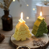 A yellow silicone Christmas tree shaped candle mold resting on a wooden surface with pine cones and cinnamon bark.