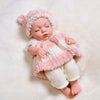 A lifelike soft vinyl reborn doll with a pink and white striped outfit and matching hat lying on a white surface.