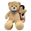 A young woman is hugging a large, light brown teddy bear plush toy.