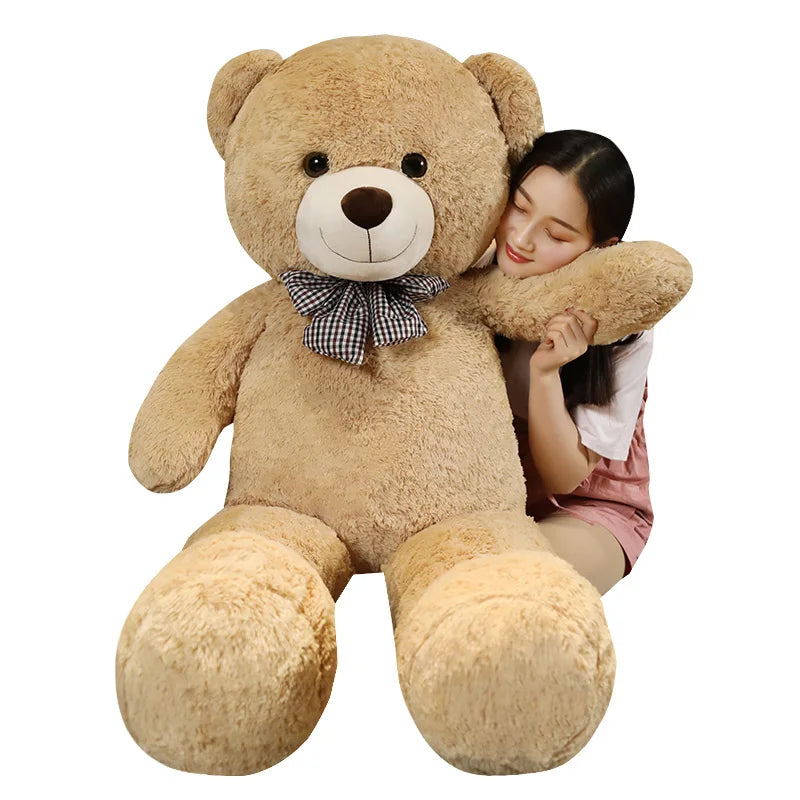 A young woman is hugging a large, light brown teddy bear plush toy.