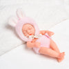 A realistic soft vinyl baby doll with a pink fuzzy hat and outfit lying on a white towel.