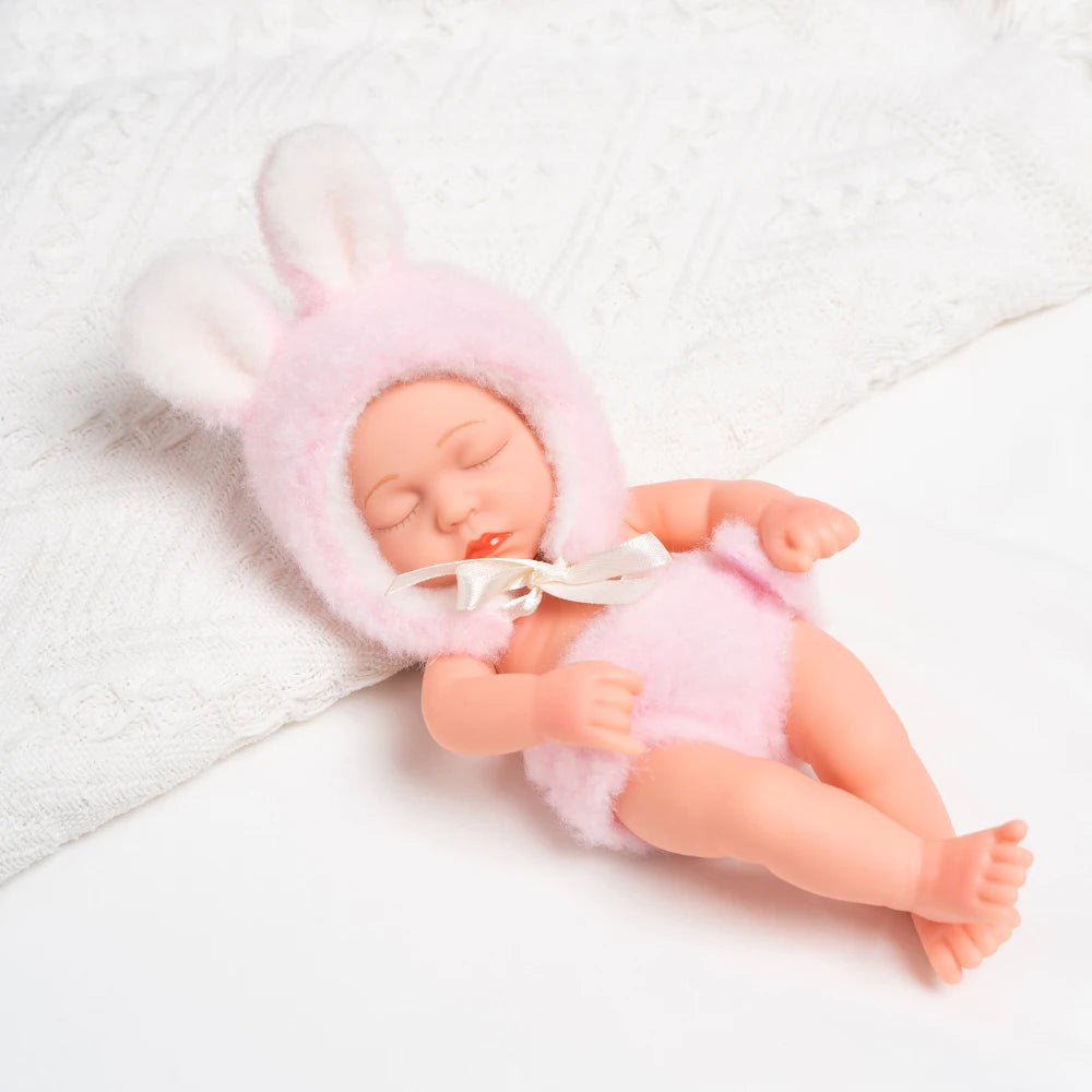 A realistic soft vinyl baby doll with a pink fuzzy hat and outfit lying on a white towel.