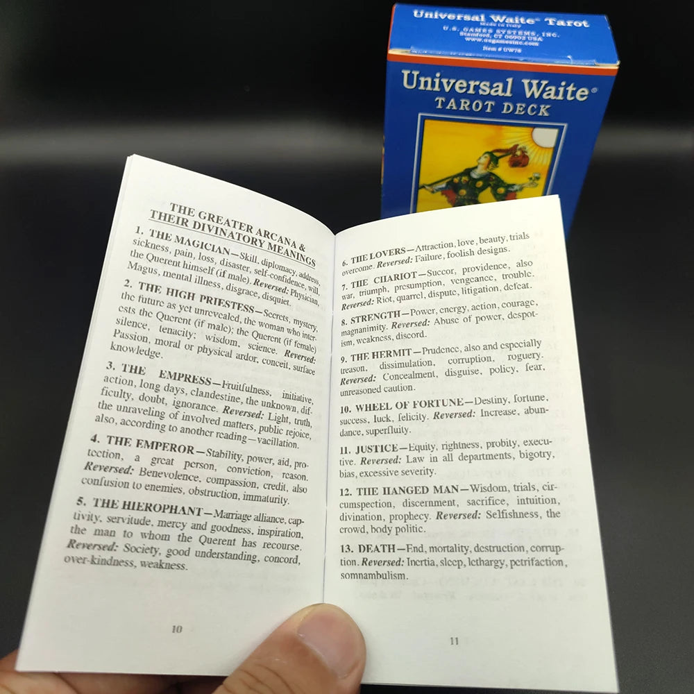 A box of Universal Waite Tarot Deck and guide book lying next to an open card, showing the back of a tarot card.