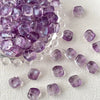 A pile of irregular square purple glass beads for jewelry making scattered on a white surface.