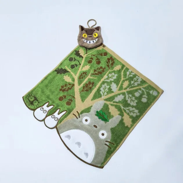 A plush toy of a cat with yellow eyes and green fur is attached to a felt leaf shape featuring a tree and small white animal 