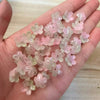 A hand holds a cluster of pink and green sakura flower crystal glass beads for jewelry making.