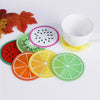 A set of colorful fruit pattern PVC coasters and a white cup are displayed on a white surface.