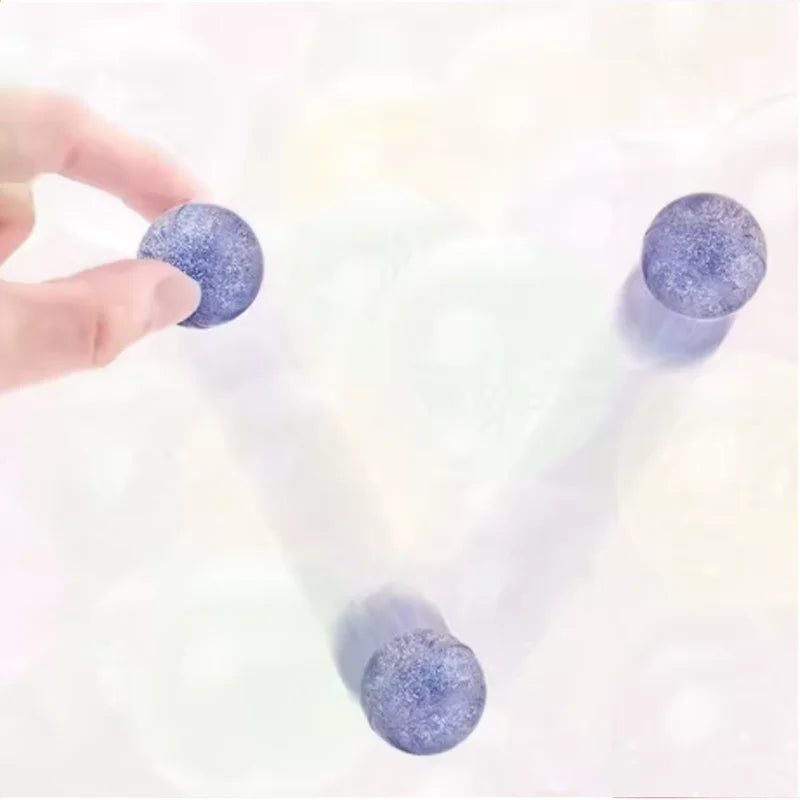 A hand is holding a purple glitter bouncy ball against a white background.