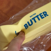 A hand is squeezing a yellow salted butter stick fidget toy with the word BUTTER visible on it.