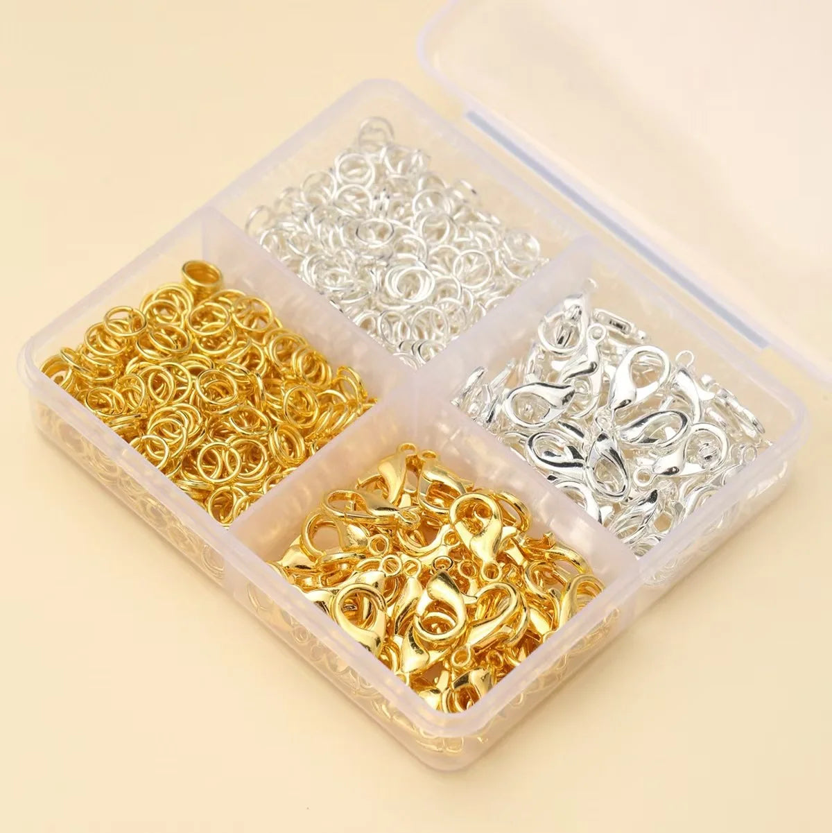 A clear plastic box containing various gold and silver lobster clasps and open jump rings for jewelry making