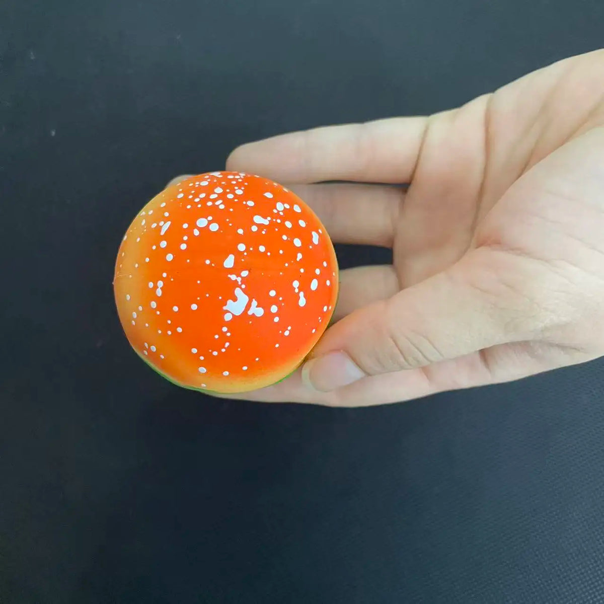 An orange squishy stress ball shaped like a hamburger with white dots