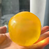 A hand is holding a smooth, translucent yellow squeezy fidget ball.