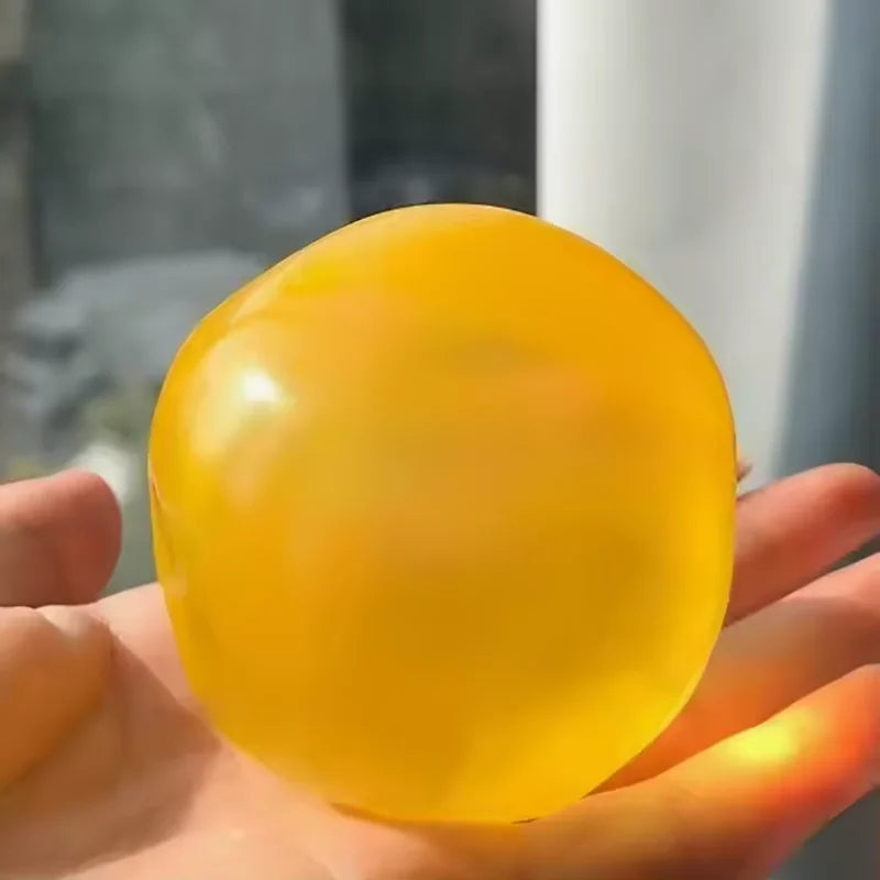 A hand is holding a smooth, translucent yellow squeezy fidget ball.