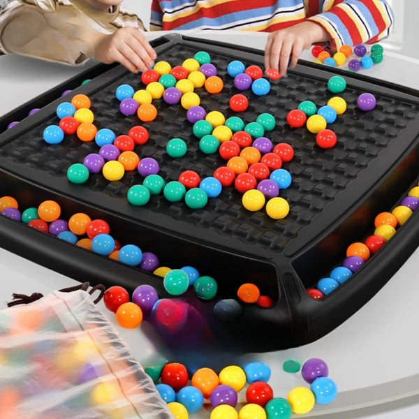 Hands are dropping colorful beads into a black plastic tray for a bead elimination game.