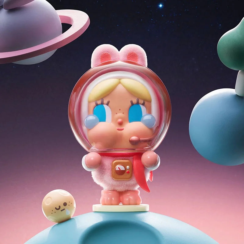 A collectible figurine of a crying baby with pink hair and blue eyes, set against a dark starry background.