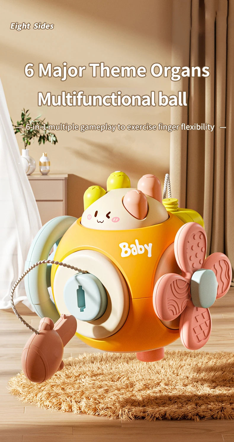 A yellow and pink multifunctional ball toy with various attachments for finger flexibility is shown on a wooden floor.
