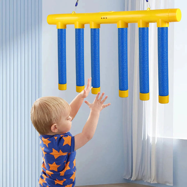 A toddler reaches for yellow and blue falling sticks hanging from a bar against a light blue wall.
