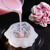 A pink liquid is poured from a glass onto a silicone mold, next to a pink floral silicone candle and resin mold.