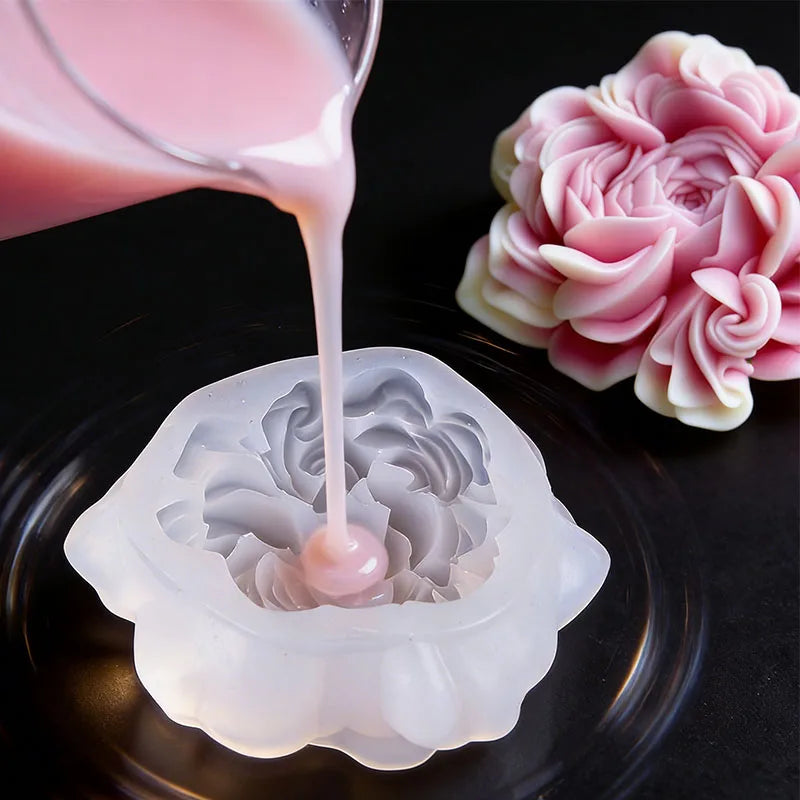 A pink liquid is poured from a glass onto a silicone mold, next to a pink floral silicone candle and resin mold.