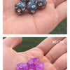 A hand holds a set of seven iridescent acrylic polyhedral dice in various colors and sizes.
