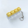 A clear acrylic keychain featuring four yellow clicky key buttons.