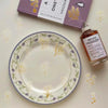 A glass plate with a floral pattern and a bottle of perfume next to a box labeled One Virginia Essays and Lettres